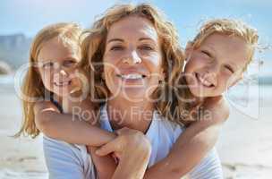 Portrait of a cheerful mature woman and little girls enjoying family time at the beach on vacation. Happy sisters smiling with adopted mother, grandma or foster parent, enjoying fresh summer air