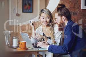 Beautiful asian woman holding a credit card and using a laptop with a handsome caucasian man in a coffee shop. Making use of the free wifi to do some shopping online. Customer convenience is the goal