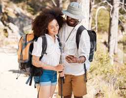 A young couple using a smartphone outdoors while on a hike in nature. Mixed race woman and african american male smiling and enjoying a n Hike in a forest while using a gps on a mobile device