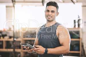 Fit gym trainer making workout programme on a tablet. Strong, muscular coach using digital tablet. Young bodybuilder using a wireless device. Masculine trainer using an online device in the gym