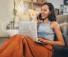 Beautiful mixed race woman using blogging laptop and cellphone to talk to clients in home living room. Hispanic entrepreneur sitting alone on floor and multitasking while networking on technology