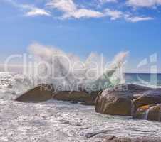 Ocean waves crashing onto a rocky beach and shore under blue sky copy space in Camps Bay, Cape Town, South Africa. Scenic seascape view of tidal sea washing over rocks, boulders on tourism attraction