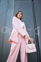 Young trendy and confident mixed race woman looking stylish while posing and chilling time in the city. Fashionable hispanic woman wearing pink clothes and a handbag, ready for an interview downtown