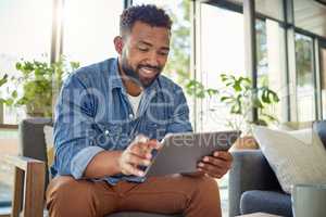 Hispanic man using his digital tablet at home. Young bachelor using his wireless device in his apartment. Handsome man browsing the internet on his digital tablet at home. Bachelor at home alone