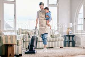 Only moms know how to juggle everything with one hand. Shot of a mom vacuuming the living room with her baby on her arm.