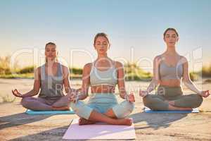 Full length yoga women meditating with legs crossed for outdoor practice in remote nature. Diverse group of mindful active friends bonding and balancing mental health. Young focused serene zen people