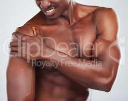 One unknown muscular fitness model experiencing shoulder pain from an injury while exercising. Black topless athlete holding his arm in pain while isolated on grey copyspace in a studio