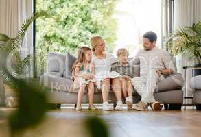Full body young smiling caucasian family embracing each other and bonding in a home living room on a weekend. Mother and father sitting with children on a sofa. Loving parents and siblings talking