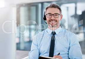 It takes patience and perseverance to make big sales. Portrait of a mature call centre agent writing notes while working on a computer in an office.