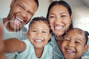 Cute little boy holding phone and taking selfie or recording funny video with his family. Happy mixed race family with two children and parents posing together for a family picture on a mobile phone