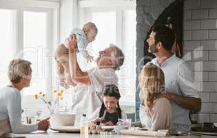 . a multi generation caucasian family bonding while spending the day together at the kitchen table at home. Grandparents being playful while holding the newborn baby. Young couple with two kids.