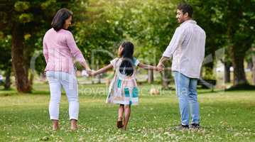 Rear view of parents and little girl holding hands while walking in park on a sunny day. Loving and caring family with one child bonding and having fun outdoors