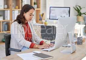 Young confident asian business woman sitting alone in an office and browsing the internet on a computer. Ambitious creative professional networking and emailing clients at a desk. Entrepreneur at work