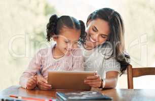Smiling mother homeschooling her daughter with a digital tablet. Mixed race woman teaching her adorable little kid at home. Cute hispanic child using technology for elearning during the covid pandemic