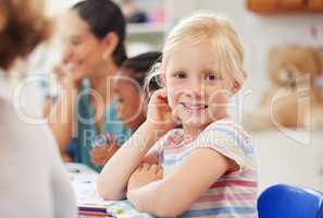 A happy little girl getting an education in primary school and learning during a lesson. Portrait of a cute, caucasian female child student sitting at a desk in class and looking at the camera