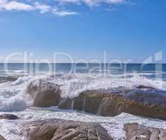 Rocks in the ocean under a cloudy blue sky with copy space. Scenic landscape of beach waves splashing against boulders or big stones in the sea at a popular summer location in Cape Town, South Africa