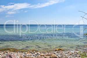 Copy space at the sea with a blue sky background. Calm ocean waves washing onto stones at an empty beach shore with sailboats cruising in the horizon. Scenic landscape for a relaxing summer holiday