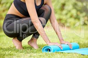 Done and dusted. an unrecognizable young woman rolling up her yoga mat after exercising outdoors.