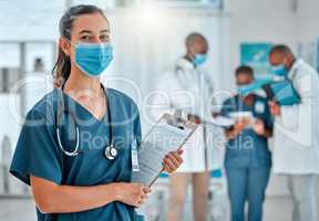 Mixed race female doctor holding a clipboard and wearing a mask while working at a hospital with colleagues. Hispanic expert medical professional ready for work at a clinic with coworkers