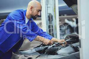 Hes an expert when it comes to engines. a handsome young male mechanic working on the engine of a car during a service.