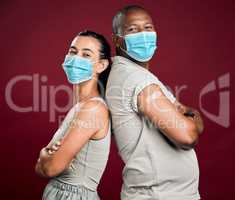 Covid vaccinated African american man and mixed race woman standing back to back. Two people wearing surgical face mask isolated against red background in studio with copyspace. Showing plaster on arm