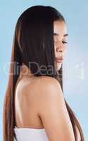 One beautiful young hispanic woman with healthy skin and sleek long hair looking over shoulder while posing against a blue studio background. Mixed race model with flawless complexion and natural beauty