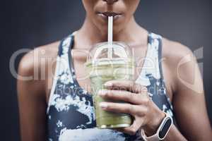 Closeup of one active woman drinking a healthy green detox smoothie while exercising outdoors. Female athlete sipping on fresh fruit juice with straw in plastic cup to cleanse and provide energy for training. Wholesome drink with vitamins and nutrients