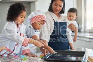 Baking gives us a creative outlet. a mother holding her baby while baking with her two children.