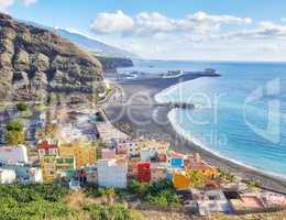 Landscape view of vibrant residential buildings, sea and ocean, a blue sky with clouds and copy space. Scenic mountain and black sand beach of coastal city of Puerto de Tazacorte in La Palma, Spain