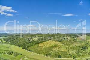 An agricultural landscape with green pasture and hill in summer. Aerial view of a farm with lush grass against a cloudy blue sky with copyspace. Peaceful farmland with calming, soothing scenic views