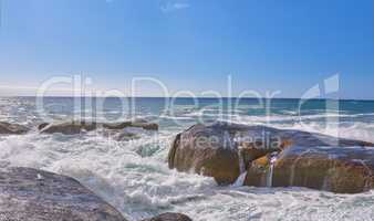 Scenic view of ocean waves and water washing over boulders and rocks in Camps Bay, Cape Town, South Africa. Empty tropical seascape with blue sky and copy space. Travel, tourism abroad and overseas