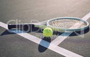 Above shot of a tennis racquet and tennis ball on a sports court. The only tools a professional tennis player needs to participate in their chosen sport. Six games per set to see who wins the match