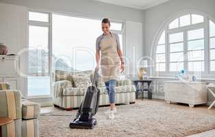 Freshening up her home. Shot of a young woman vacuuming a carpet in the lounge at home.