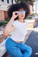 Young stylish mixed race woman with curly natural afro hair wearing trendy glasses outside. One female only looking carefree, cool and confident. Happy fashionable hispanic woman relaxing in the city