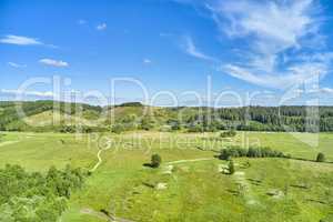 Landscape of a countryside with a cloudy blue sky and copyspace. Wide drone view of green forestry and cultivated grassland. Beautiful landscape of flat land surrounded by forest trees with copyspace