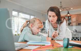 Adorable little caucasian girl sitting at table and doing homework while her mother helps her. Beautiful serious young woman pointing and teaching her daughter at home. Parent home schooling her child