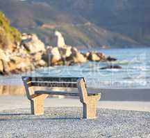 Beautiful relaxing view of the ocean with a bench at the beach on a summer day. The landscape of the sea shore with big rocks and calm waves on a peaceful spring afternoon on the coastline