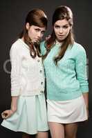 Pretty in pastels. Studio shot of two attractive young women dressed up in 60s wear against a dark background.