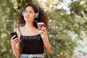 One young mixed race woman enjoying the city and using her cellphone to listen to music through headphones while drinking a takeaway coffee. Hispanic woman browsing the internet on a phone downtown