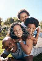 Happy african american family of four lying stacked on top of each other while having fun and playing together in the sun. Carefree mother and two kids piled on top of father while bonding at the park