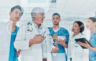 There are many changes happening, and we need to keep up. a group of medical practitioners brainstorming with notes on a glass wall in a medical office.