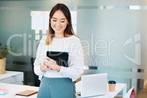 Ticking tasks off one by one. an attractive young businesswoman standing alone in the office and holding a digital tablet.