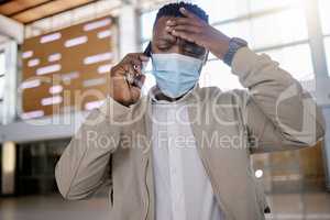 African american male on a phone call with his mobile device inside a station during the day while wearing a mask. Young black male talking on a phone while commuting in a train station and looking stressed