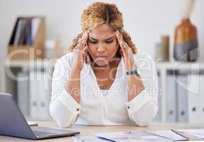 Young mixed race businesswoman suffering from a headache while sitting at a desk in an office at work. One stressed hispanic businessperson suffering from anxiety and looking upset