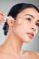 One beautiful mixed race woman using a rose quartz derma roller during a selfcare grooming routine. Young hispanic woman using anti ageing tool against grey copyspace background