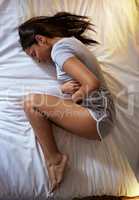I can barely move. Full length shot of an attractive young woman lying alone on her bed and suffering from a tummy ache.