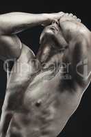 Chiseled. Monochrome shot of a muscular young man posing nude in studio against a dark background.