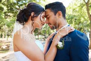 Bride and groom standing together and touching foreheads while standing together on their wedding day. Newlywed couple sharing romantic moment outdoors