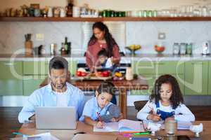 Family working at a kitchen table, doing homework at home. A young man using a laptop next to his children. A little boy and girl playing while their father is online. Remote learning in quarantine