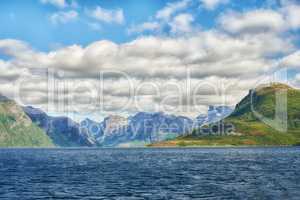 Landscape of mountains north of polar and arctic circle in Bodo, Norway. Scenic view of green hills surrounded by ocean in remote area with clouds. Traveling abroad, overseas for holiday and vacation